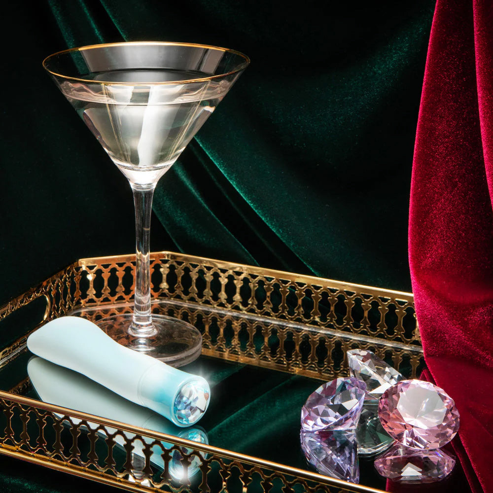 Singapore Blush Oh My Gem blue vibe displayed on a gold tray beside a martini glass and scattered crystals—blending luxury and intimate empowerment for non-binary, femme, and trans users.