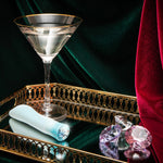 Singapore Blush Oh My Gem blue vibe displayed on a gold tray beside a martini glass and scattered crystals—blending luxury and intimate empowerment for non-binary, femme, and trans users.