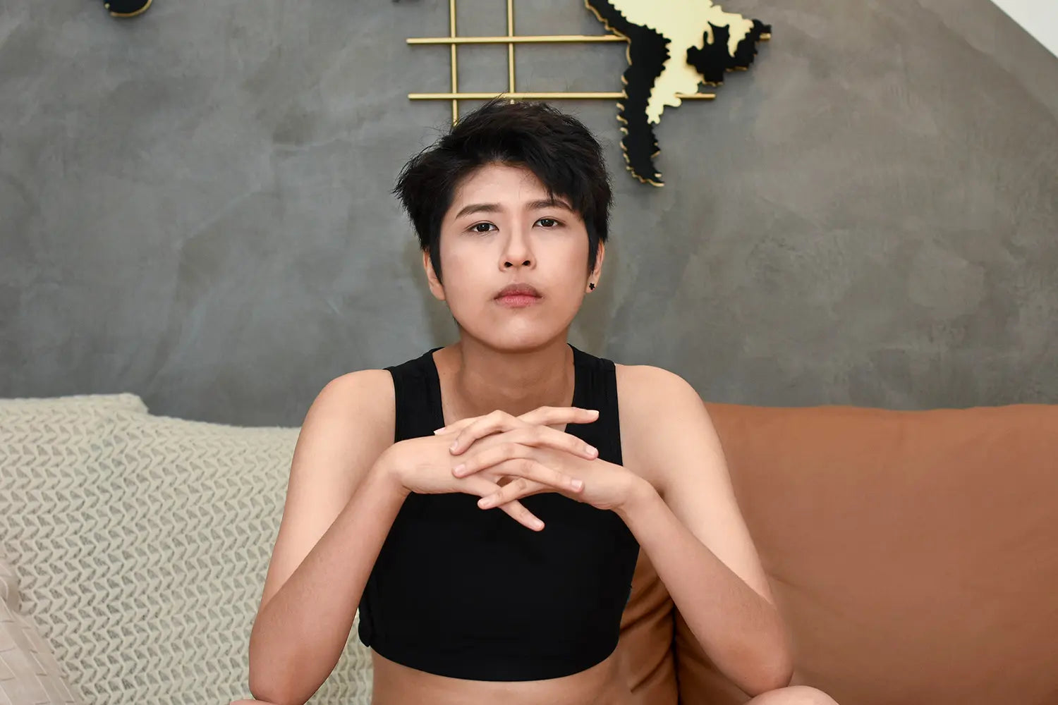 A proud lesbian model reclines casually on a couch, wearing TOMSCOUT’s black chest binder and exuding unapologetic femininity and body positivity in a chic, relaxed setting.