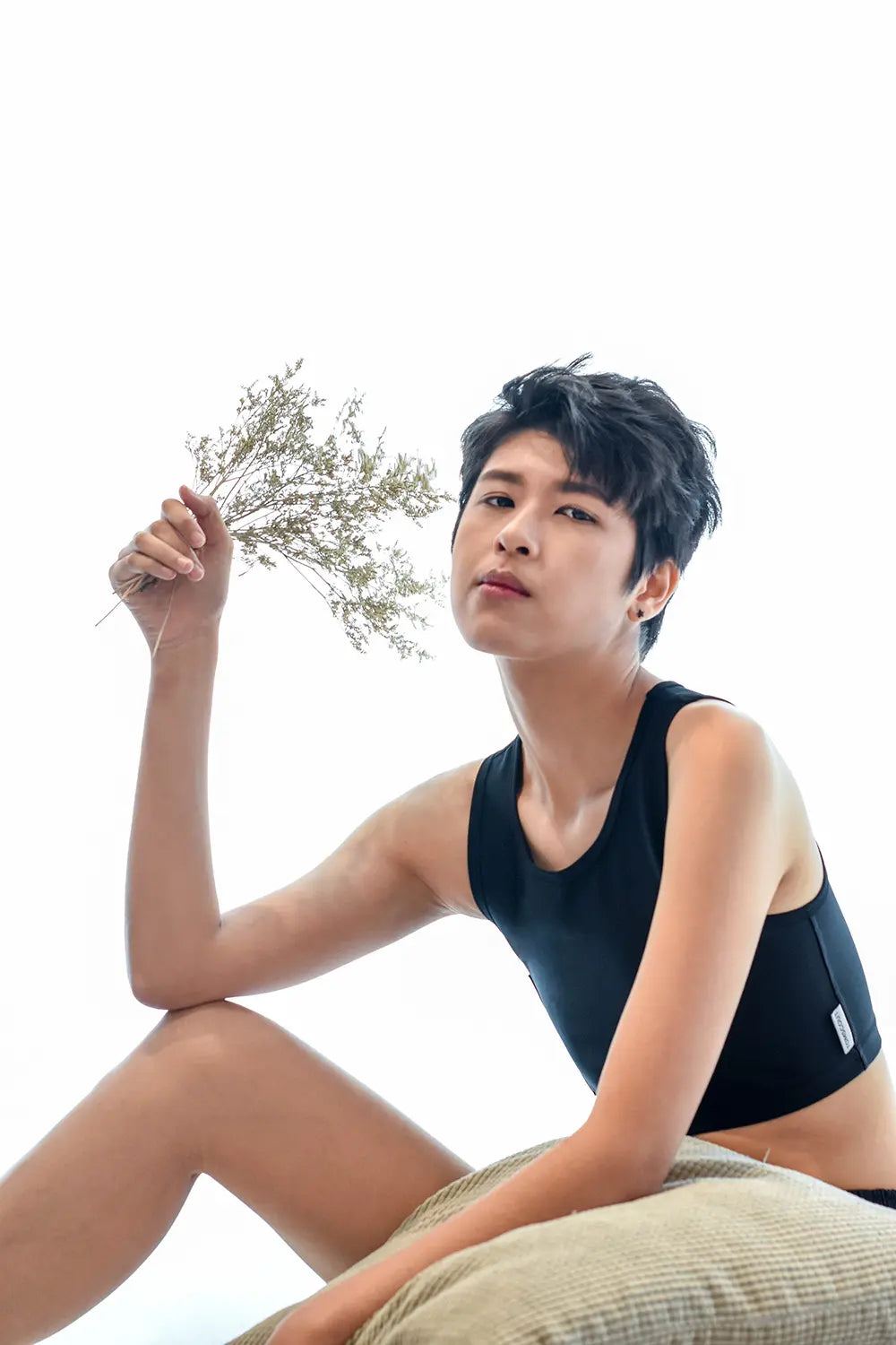A lesbian model in a sleek black TOMSCOUT binder holds a sprig of wildflowers, combining soft natural elements with bold gender expression, radiating empowerment and self-love.