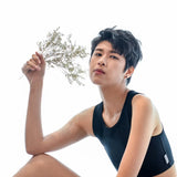 A lesbian model in a sleek black TOMSCOUT binder holds a sprig of wildflowers, combining soft natural elements with bold gender expression, radiating empowerment and self-love.