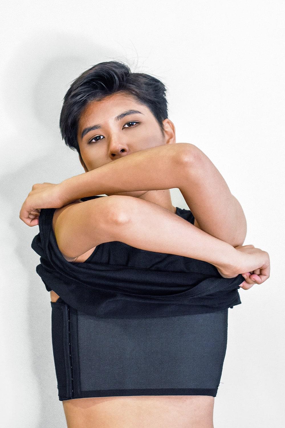 FTM individual lifting their shirt to reveal a sleek black TOMSCOUT chest binder with side hook closures and flat compression, designed for gender euphoria, breathable comfort, and discreet wear under any outfit.