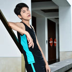 Androgynous person leans casually against a golden railing in a modern poolside setting, showcasing the athletic cut and vibrant side stripes of the TOMSCOUT swim binder and matching shorts.