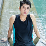 Tomboy relaxes in the shallow end of a sunlit pool wearing a TOMSCOUT chest binder swim set, the sleek black and teal design clinging comfortably to their body for a flat, affirming silhouette.