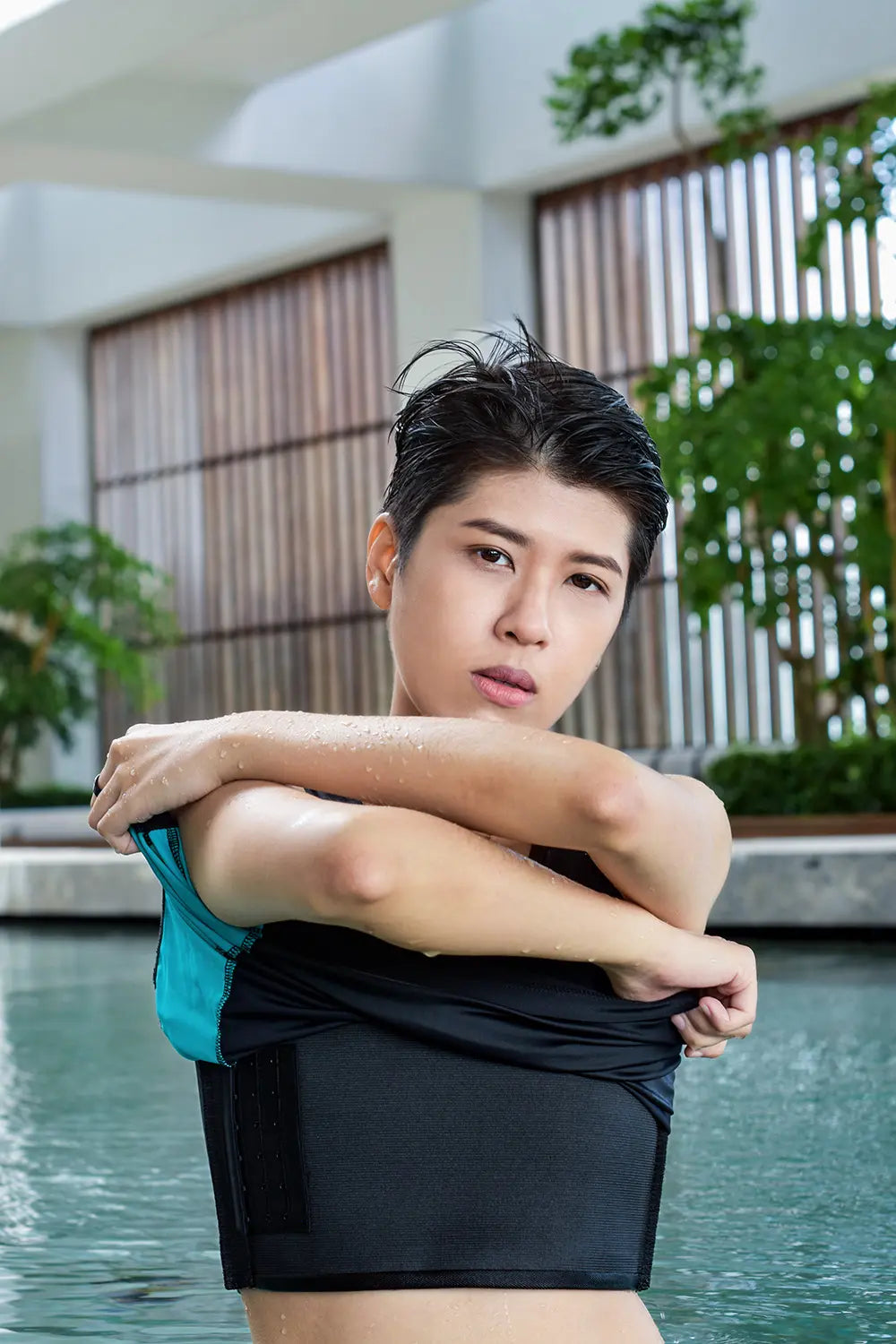 Non-binary model lifts a TOMSCOUT swim top to reveal a secure, high-compression black binder underneath, highlighting the gender-affirming fit and moisture-wicking fabric for water activity confidence.
