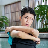 Non-binary model lifts a TOMSCOUT swim top to reveal a secure, high-compression black binder underneath, highlighting the gender-affirming fit and moisture-wicking fabric for water activity confidence.