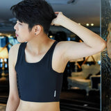 An FTM individual stands against a mirrored wall, gazing outward in a form-fitting TOMSCOUT chest binder—highlighting strong posture and gender-affirming confidence in a chic, athletic cut.