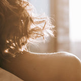 Artistic close-up of a bare shoulder and tousled hair bathed in golden light, symbolizing tender, gender-affirming self-love and body intimacy supported by HARU’s gentle lubricants.