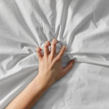 Sensual close-up of a hand gripping white bedsheets, evoking queer erotic pleasure and intimacy enhanced by silky, body-safe lubricants like HARU.