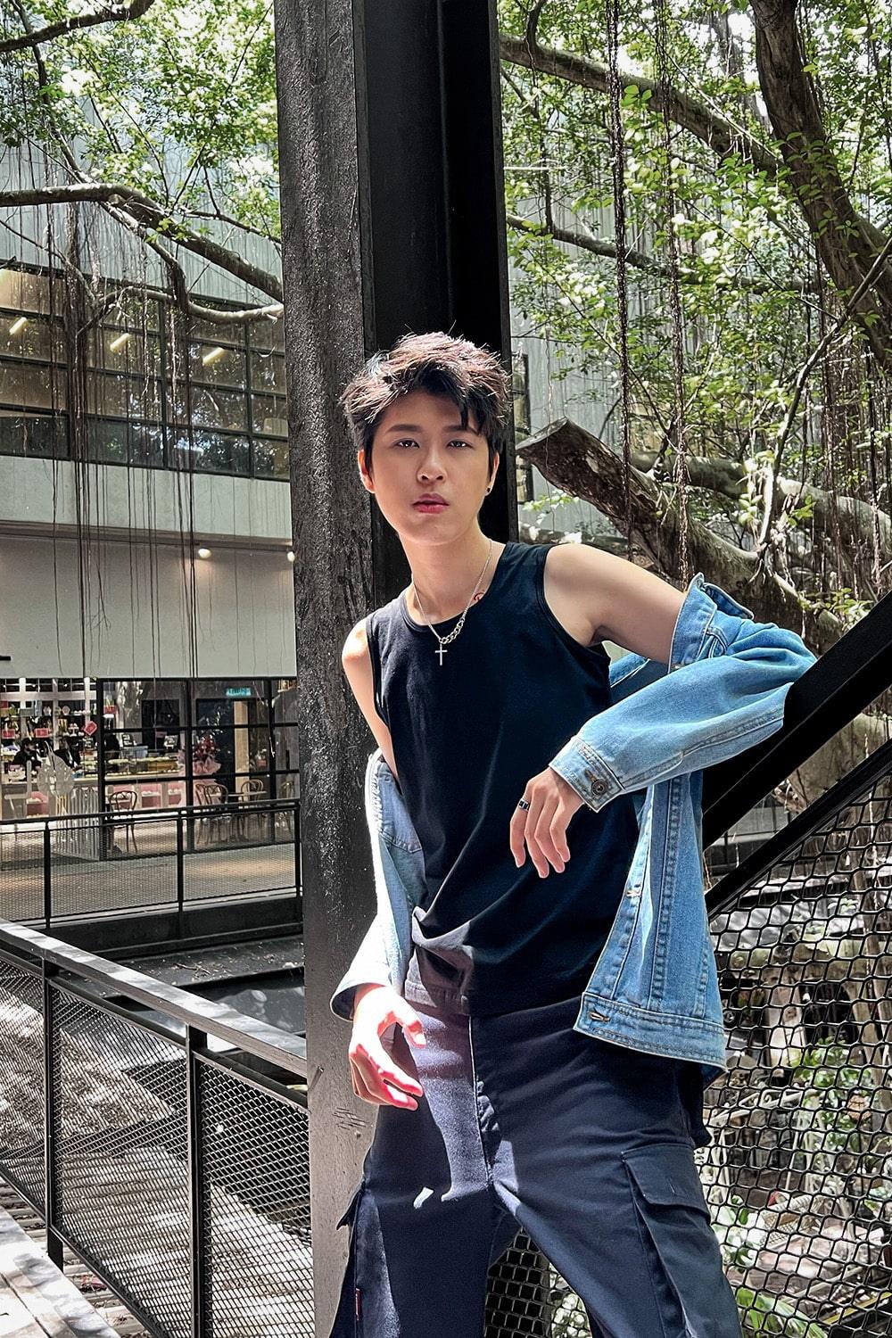 Trans masc-presenting model stands poised against a metal railing, wearing TOMSCOUT’s gender-affirming black chest binder and rugged navy cargo pants, blending street style with soft rebellion in a lush, open-air setting.