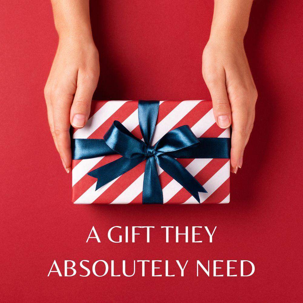 Hands holding a red and white striped gift box tied with a navy blue ribbon against a bold red background, with the text “A Gift They Absolutely Need”—perfect visual for TOMSCOUT’s digital gift card, ideal for birthdays, holidays, or gender-affirming milestones.