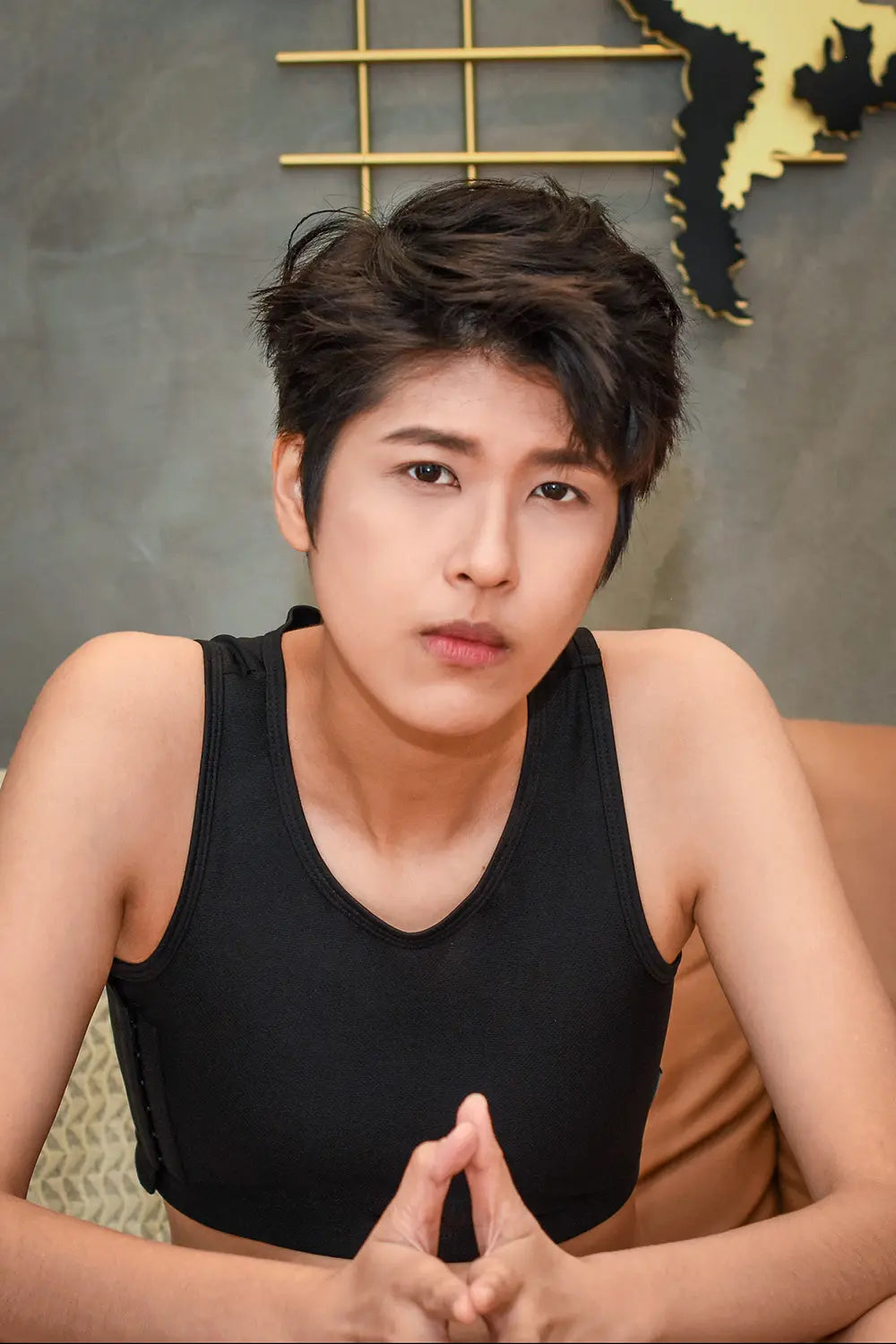A trans man with short, tousled black hair gazes thoughtfully into the distance while wearing a TOMSCOUT chest binder in classic black, exuding confidence and gender-affirming style.