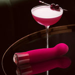 Singapore Blush Oh My Gem “Classy” G-spot vibrator in deep burgundy placed beside a rich pink cocktail with cherries, evoking indulgence and sensuality for lesbian and tomboy pleasure seekers.