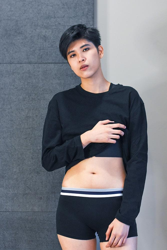 Androgynous model wearing black TOMSCOUT boxer briefs with a sleek navy and white waistband, paired with a cropped black top. The ultra-soft stretch cotton hugs the hips without riding up—perfect for non-binary folks seeking body-affirming essentials with minimal seams and maximum confidence.