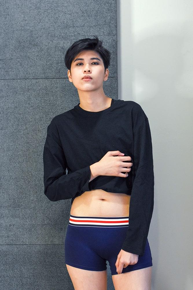 Androgynous model wearing navy boxer briefs with a red, white, and blue waistband, paired with a black crop top. The gender-neutral silhouette highlights TOMSCOUT’s inclusive underwear line—soft, stretchy, and built for comfort and dysphoria-safe style.