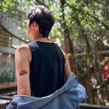 FTM-presenting person showing off a rainbow pride tattoo on their upper arm while wearing a sleeveless black top—TOMSCOUT’s unapologetic celebration of trans pride and outdoor confidence.