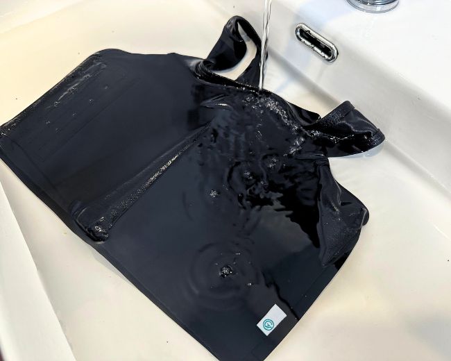 Close-up of TOMSCOUT chest binder being hand-washed, highlighting logo tag and durable stitching.