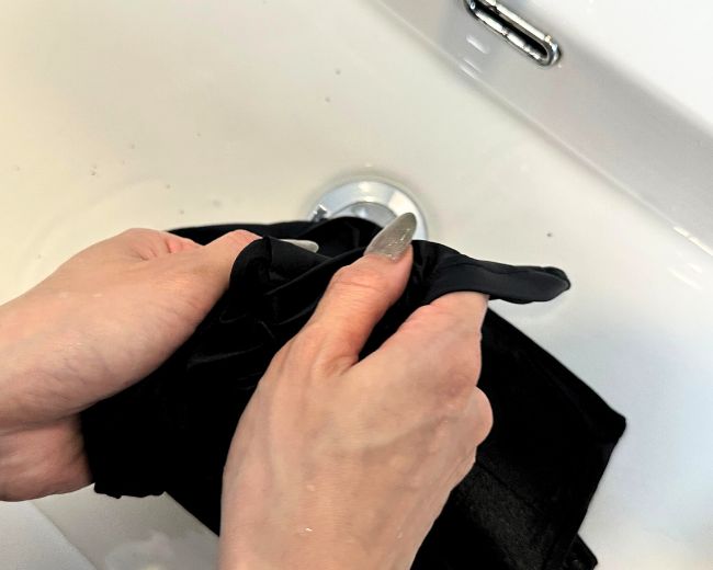 Hand washing a TOMSCOUT chest binder in a sink—recommended for spot-cleaning or delicate care routines.