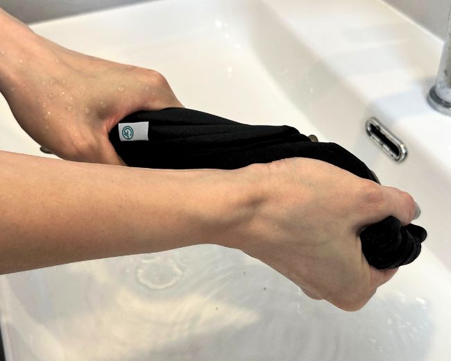 Gently wringing excess water from a TOMSCOUT chest binder—avoid twisting to protect binder integrity.