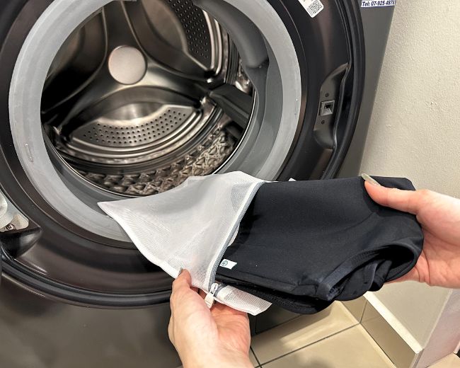 Placing a TOMSCOUT chest binder into a protective mesh laundry bag—recommended step to prevent damage during machine washing.