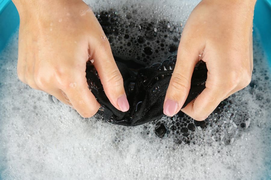 Hands gently washing a chest binder with soapy bubbles, showcasing the correct technique for binder maintenance and care.