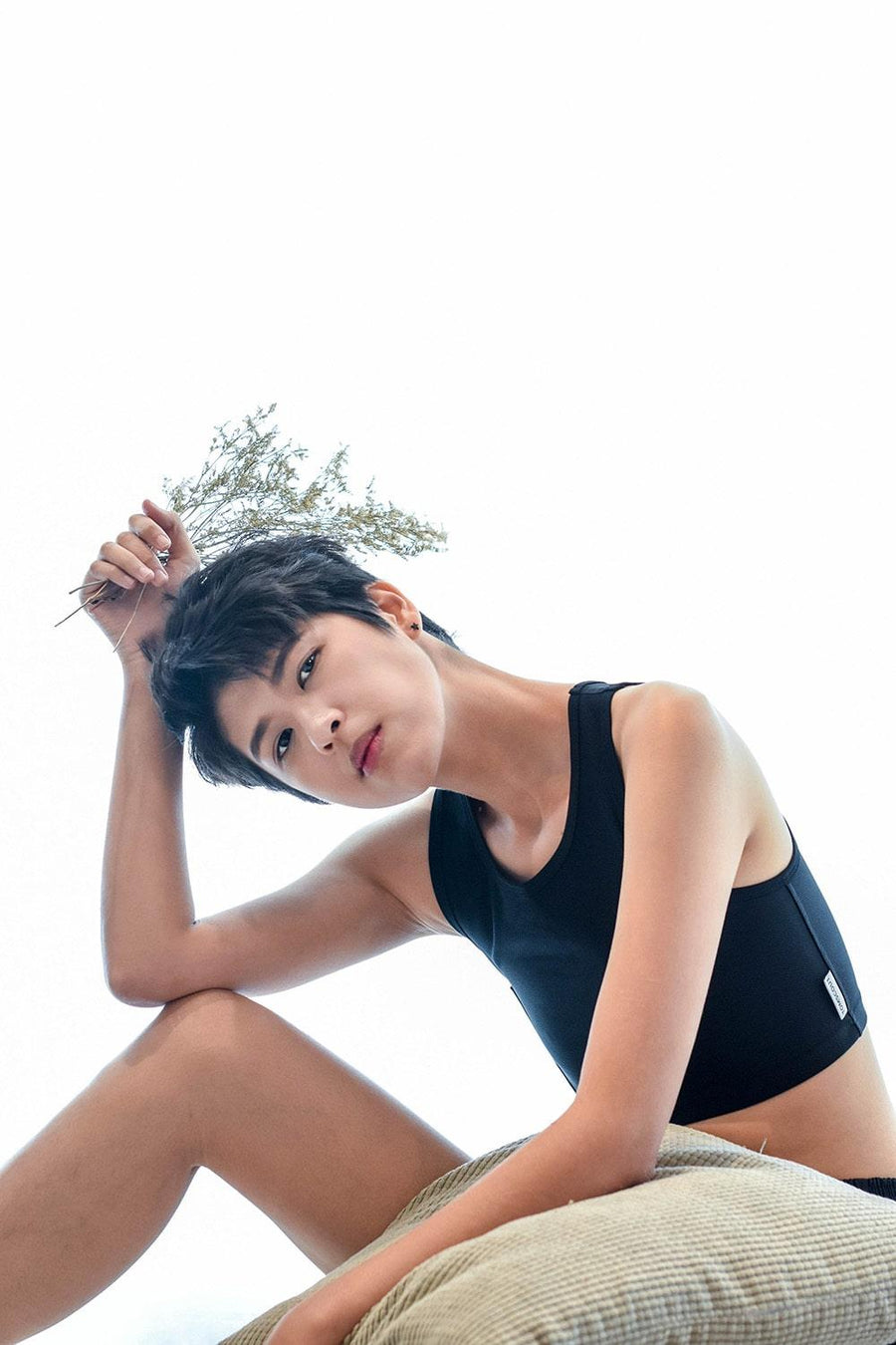 A non-binary androgynous tomboy, transgender man sitting and holding a flower as prop and wearing a black color of a non-bandage TOMSCOUT Chest Binder to fight body dysphoria and looking confidence towards the camera. TOMSCOUT BECOMING non-bandage binder.