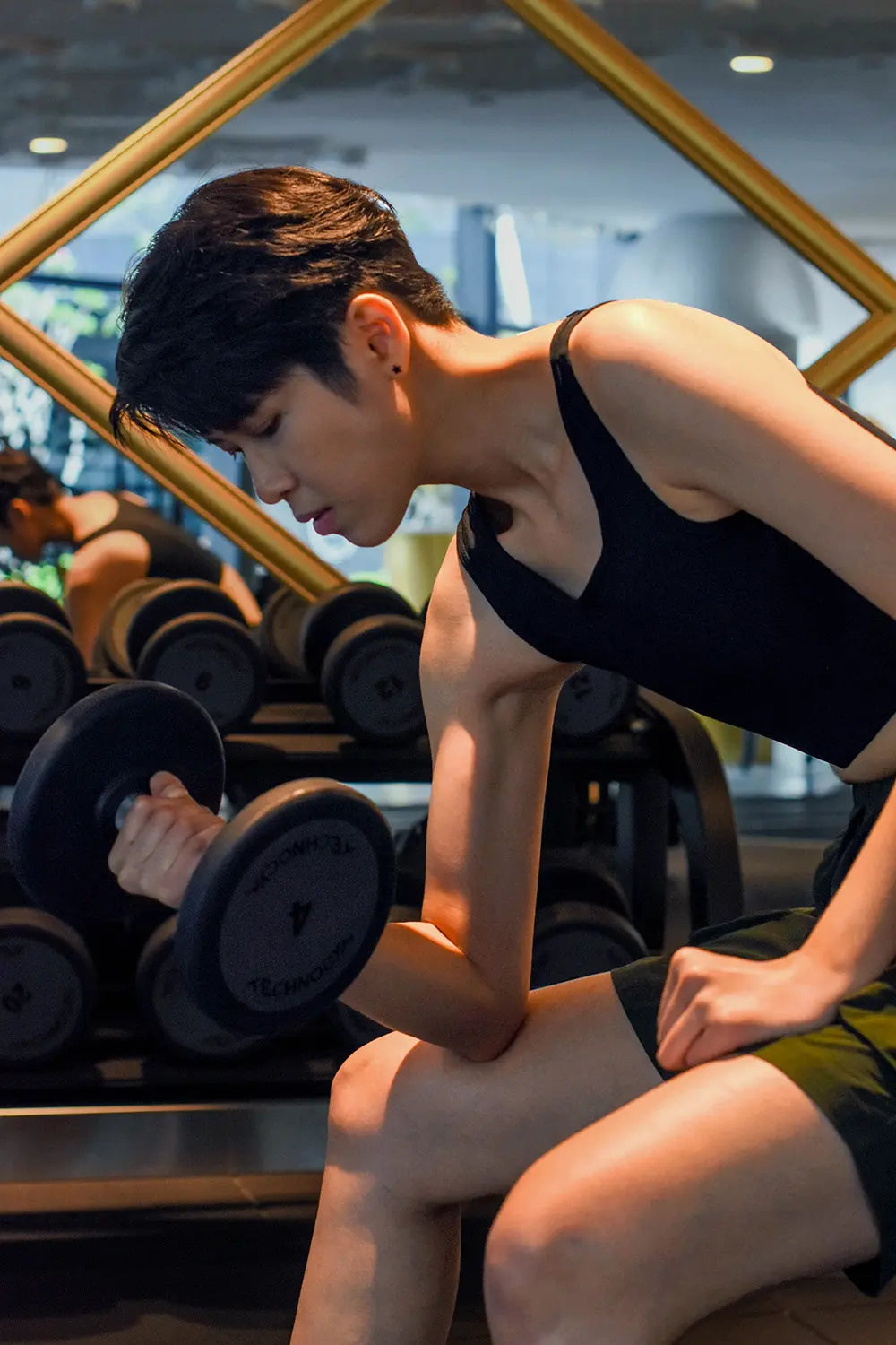 Focused and powerful, a tomboy lifter curls a dumbbell while wearing a black TOMSCOUT binder, designed to stay securely in place during intense gym sessions without compromising comfort.