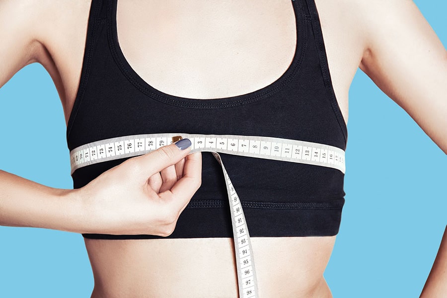 Close-up of a non-binary person measuring their chest with a soft tape measure over a black sports bra—offering a practical, affirming visual on how to get the right TOMSCOUT binder size at home with confidence.