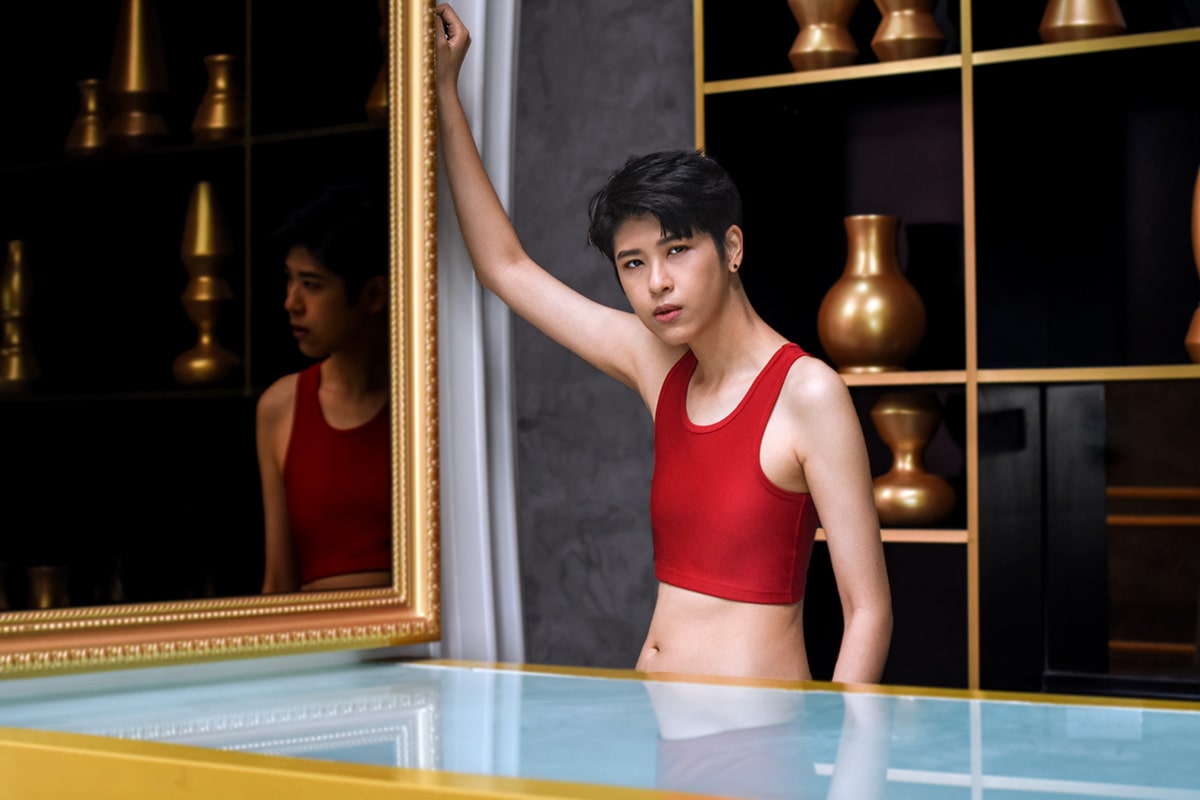 A non-binary androgynous tomboy transman lesbian in a TOMSCOUT scarlet red Chest Binder, exemplifying the fight against body dysphoria and the elation of gender euphoria with a flattened chest. Showcased in the TOMSCOUT Free Chest Binder Program, The Freedom Binder.