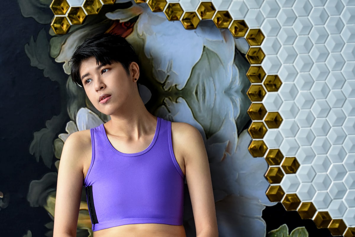 A non-binary androgynous tomboy transman lesbian wearing a TOMSCOUT lavender purple color Chest Binder to fight body dysphoria and experience the joy of gender euphoria with a flattened chest. TOMSCOUT Free Chest Binder Program, The Freedom Binder