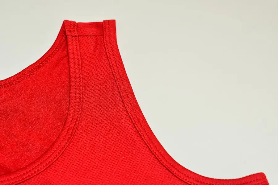 Close-up of the neckline and shoulder strap on a red TOMSCOUT compression binder, featuring double-stitched seams and a racerback cut for added durability and freedom of movement. Designed with soft, sweat-wicking mesh, this binder empowers tomboy-identifying wearers to move confidently and comfortably in any setting. Included in the Free Chest Binder Program for gender-diverse youth and adults.