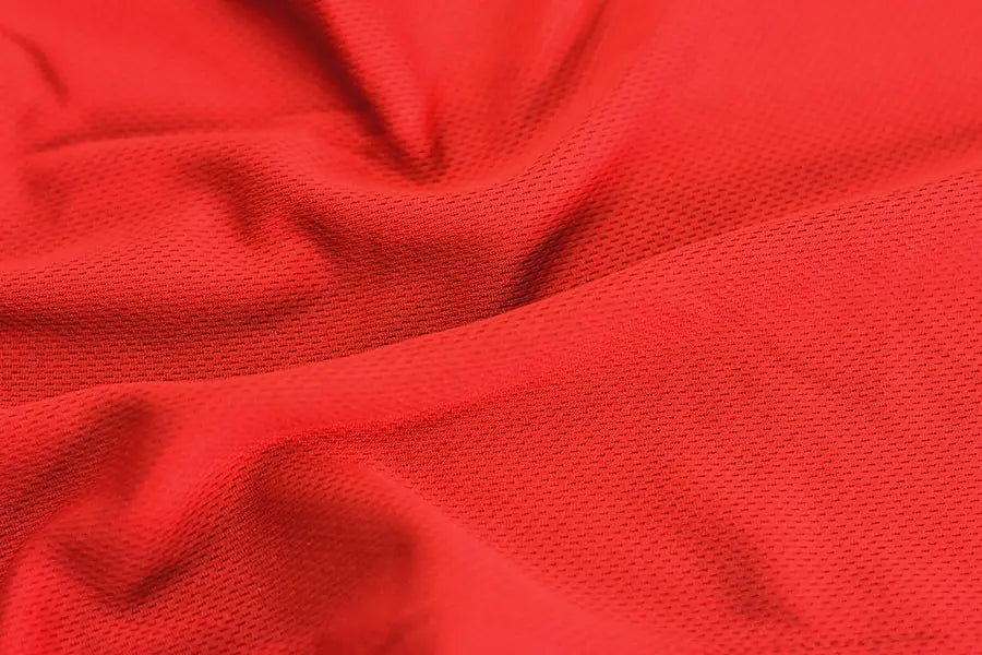 Macro shot of TOMSCOUT’s signature red mesh binder fabric, showcasing its ultra-breathable, four-way stretch texture. Engineered for lesbians and queer women seeking cool, lightweight compression, this moisture-wicking material offers both softness and structure—ideal for all-day wear, workouts, or layering under streetwear. Proudly part of the Free Chest Binder Program for accessibility and empowerment.