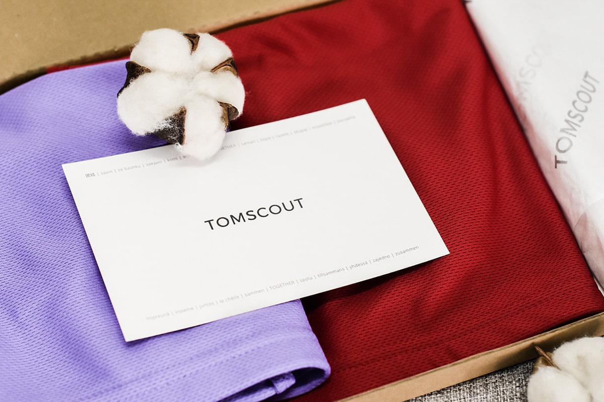 Inside a gift box, two Chest Binders in lavender purple and scarlet red colors are neatly arranged alongside a TOMSCOUT inspirational thank you card, symbolizing wholehearted support for the LGBTQ community. TOMSCOUT Free Chest Binder Program, The Freedom Binder
