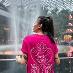 Asian female with long hair elegantly dressed in a hot pink t-shirt, embellished with a classic batik orchid flower embroidery, complemented by an array of LGBT rainbow pride accessories and a sustainable bracelet. Part of the TOMSCOUT Flourish - LGBT Pride Kits, capturing the essence of pride and style in Jewel Changi Airport Singapore.