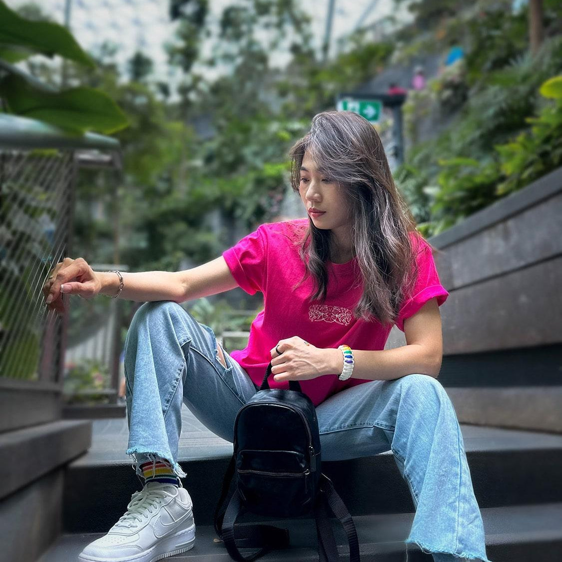 Asian female with long hair elegantly dressed in a hot pink t-shirt, embellished with a classic batik orchid flower embroidery, complemented by an array of LGBT rainbow pride accessories and a sustainable bracelet. Part of the TOMSCOUT Flourish - LGBT Pride Kits, capturing the essence of pride and style in Jewel Changi Airport Singapore.