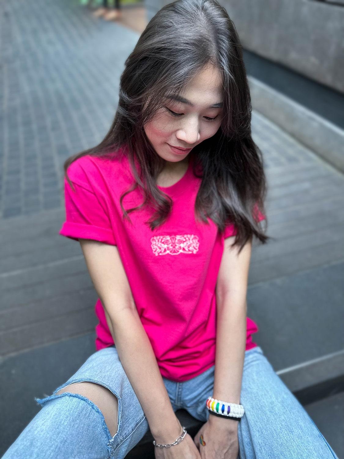 An Asian female with long hair is wearing a hot pink t-shirt adorned with an embroidery design of the classic batik orchid flower on the front. TOMSCOUT Flourish - LGBT Pride Kits (Singapore)