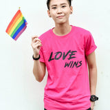 An Asian tomboy with clean hair cut is wearing a hot pink t-shirt with the love wins wording at the front and holding a small pride flag. TOMSCOUT Flourish - LGBT Pride Kits (Singapore)