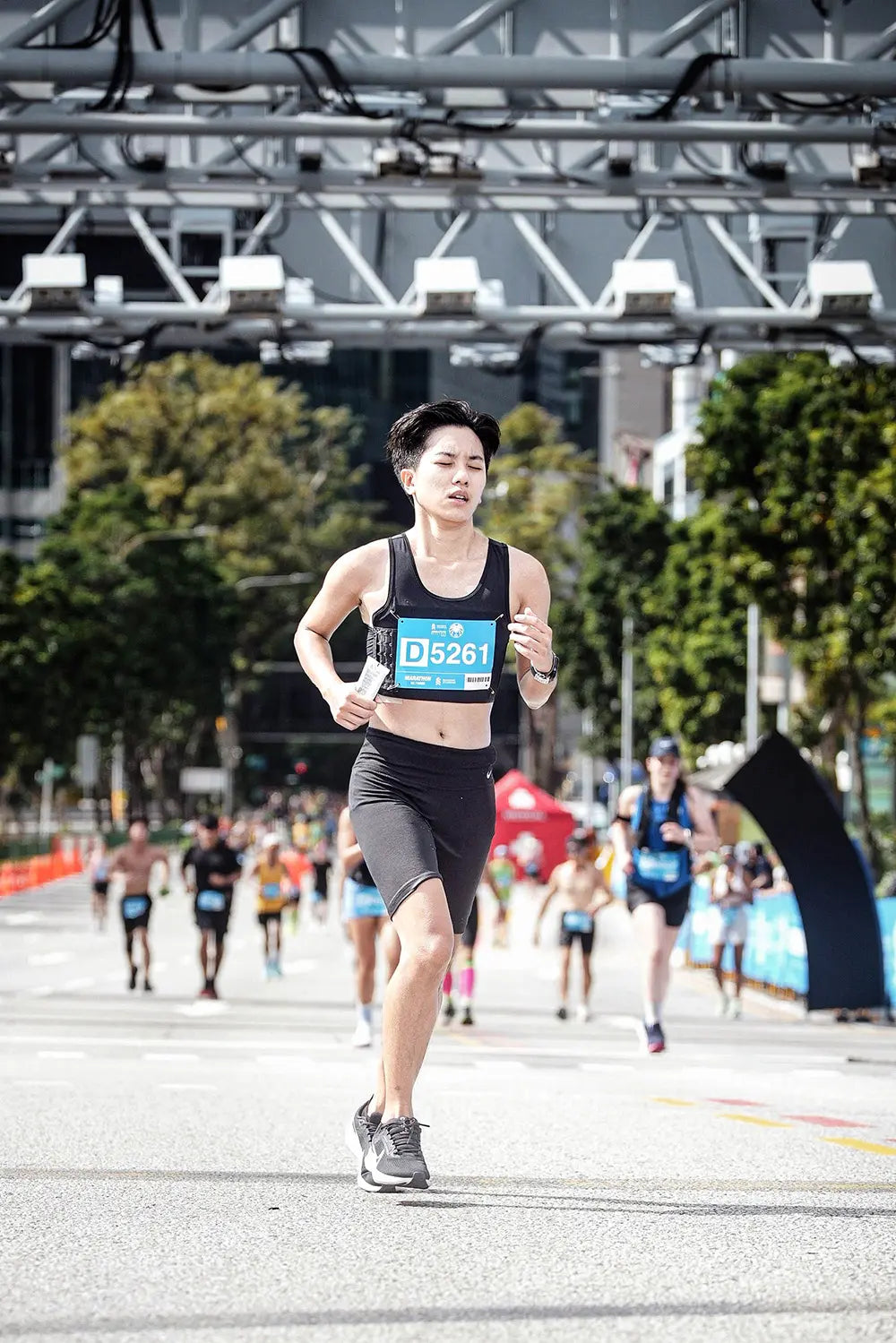 A determined FTM athlete running a city marathon in a TOMSCOUT chest binder and compression shorts, captured mid-stride under bright daylight, radiating strength, endurance, and gender-affirming pride.