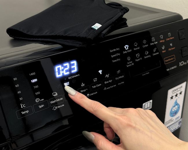 Finger pressing gentle 23-minute wash cycle on the machine—ideal washing mode to preserve chest binder durability and elasticity.