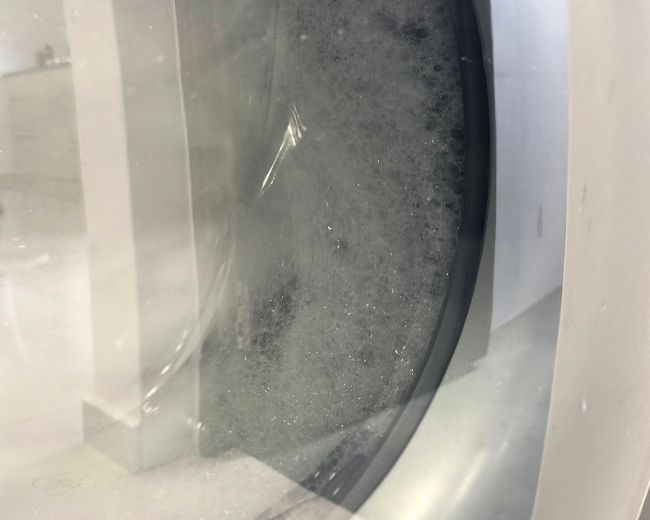 TOMSCOUT chest binder inside front-load washing machine with visible soap suds—gentle cleaning in progress.