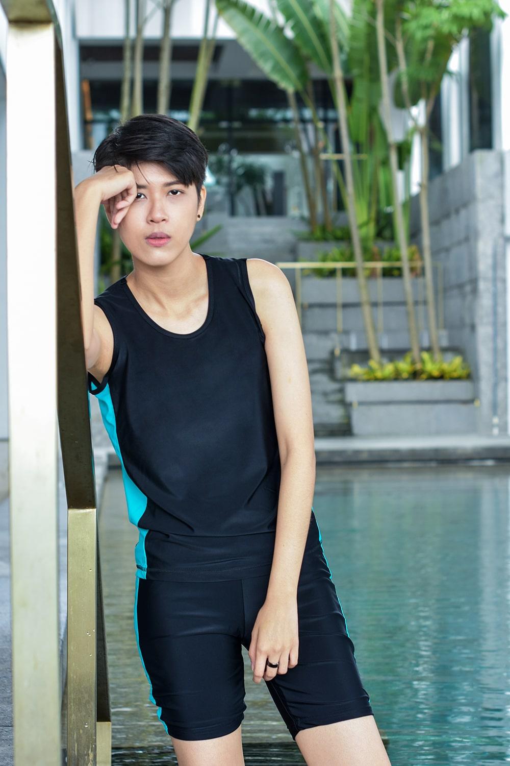 A non-binary androgynous tomboy, transgender man wearing a black color of a bandage TOMSCOUT Swimming Chest Binder to fight body dysphoria and swimming in the pool, TOMSCOUT SAPPHIRE SWIMMING BINDER.