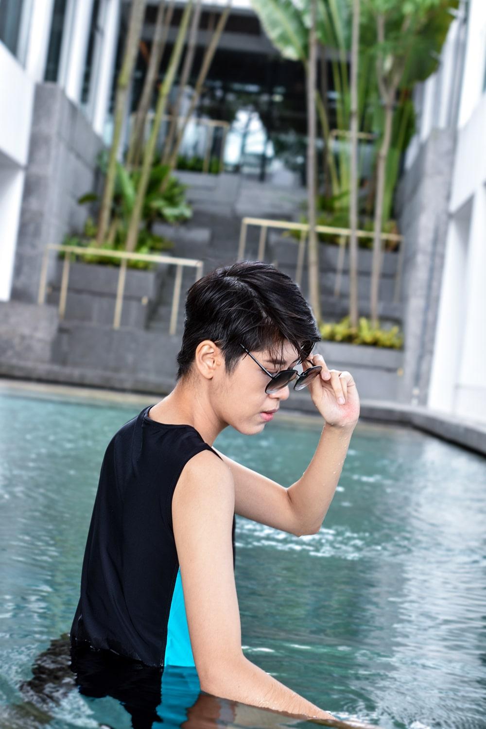 A non-binary androgynous tomboy, transgender man wearing a black color of a bandage TOMSCOUT Swimming Chest Binder to fight body dysphoria and swimming in the pool, TOMSCOUT SAPPHIRE SWIMMING BINDER.