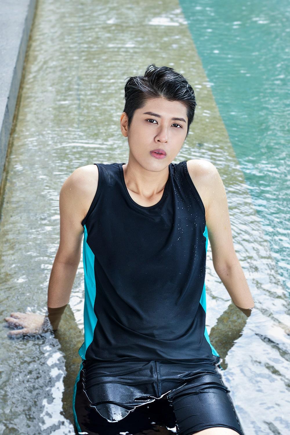 A non-binary androgynous tomboy, transgender man wearing a black color of a bandage TOMSCOUT Swimming Chest Binder to fight body dysphoria and swimming in the pool, TOMSCOUT SAPPHIRE SWIMMING BINDER.