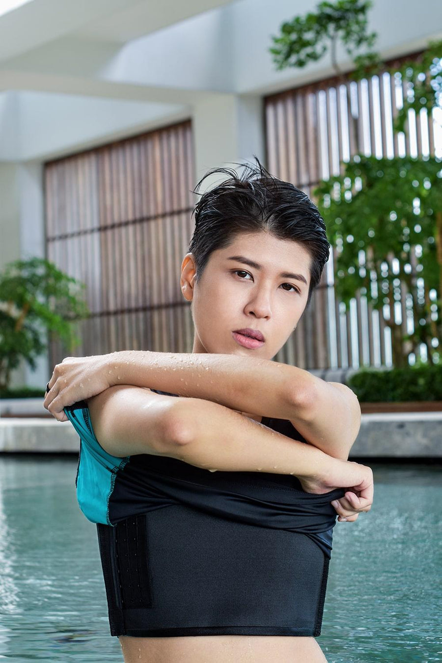 A non-binary androgynous tomboy, transgender man wearing a black color of a bandage TOMSCOUT Swimming Chest Binder to fight body dysphoria and swimming in the pool, TOMSCOUT SAPPHIRE SWIMMING BINDER.