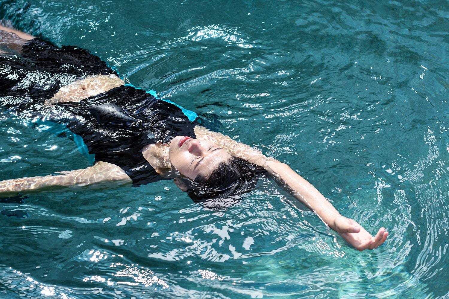 A non-binary androgynous tomboy, transgender man wearing a black color of a bandage TOMSCOUT Swimming Chest Binder to fight body dysphoria and swimming in the pool, TOMSCOUT SAPPHIRE SWIMMING BINDER.