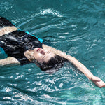 A non-binary androgynous tomboy, transgender man wearing a black color of a bandage TOMSCOUT Swimming Chest Binder to fight body dysphoria and swimming in the pool, TOMSCOUT SAPPHIRE SWIMMING BINDER.