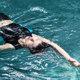 A non-binary androgynous tomboy, transgender man wearing a black color of a bandage TOMSCOUT Swimming Chest Binder to fight body dysphoria and swimming in the pool, TOMSCOUT SAPPHIRE SWIMMING BINDER.
