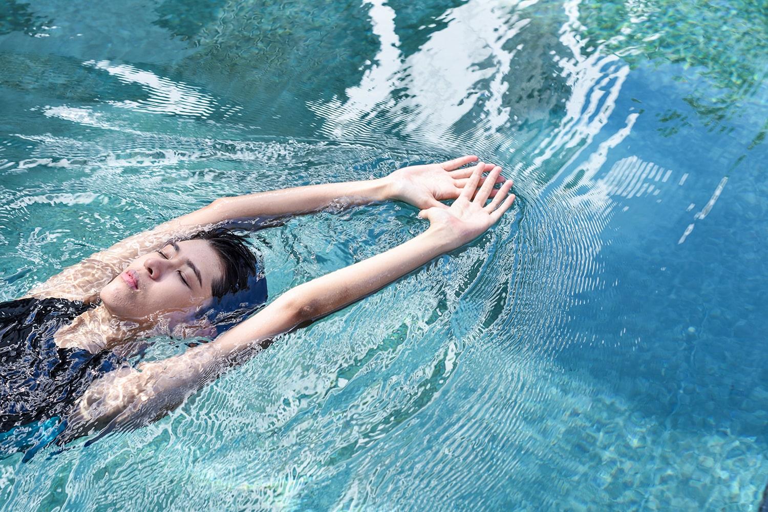 A non-binary androgynous tomboy, transgender man wearing a black color of a bandage TOMSCOUT Swimming Chest Binder to fight body dysphoria and swimming in the pool, TOMSCOUT SAPPHIRE SWIMMING BINDER.