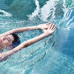 A non-binary androgynous tomboy, transgender man wearing a black color of a bandage TOMSCOUT Swimming Chest Binder to fight body dysphoria and swimming in the pool, TOMSCOUT SAPPHIRE SWIMMING BINDER.
