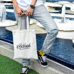 A non-binary androgynous tomboy, transgender man holding a white color embroidered Be Kind canvas tote bag with the LGBTQ+ pride black color design. TOMSCOUT BE KIND - Tote Bag